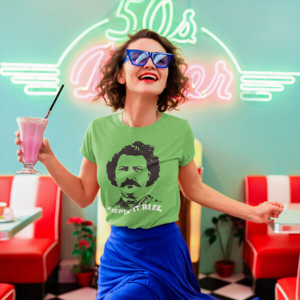 A happy looking human holds a milkshake while wearing a green shirt with a picture of Louis Riel and the words "Keepin' It Riel"